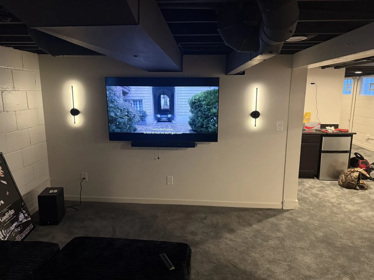 Large flat-screen TV professionally mounted on a basement wall with cables concealed and accent sconces